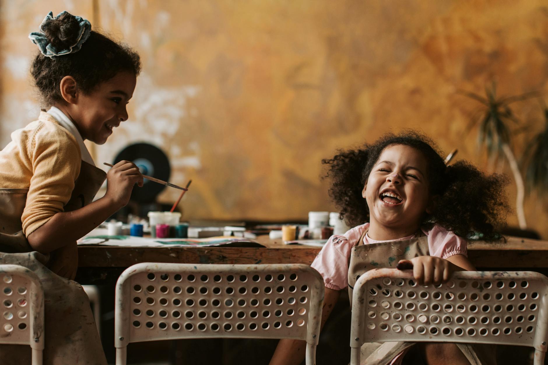 Dwoje dzieci w fartuszkach maluje farbami przy stole w domu