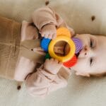 Ząbkowanie a rozwój: czy marudzenie i gorszy sen mogą wpływać na postępy? Niemowlę leżące na kocu gryzie kolorowy gryzak podczas ząbkowania