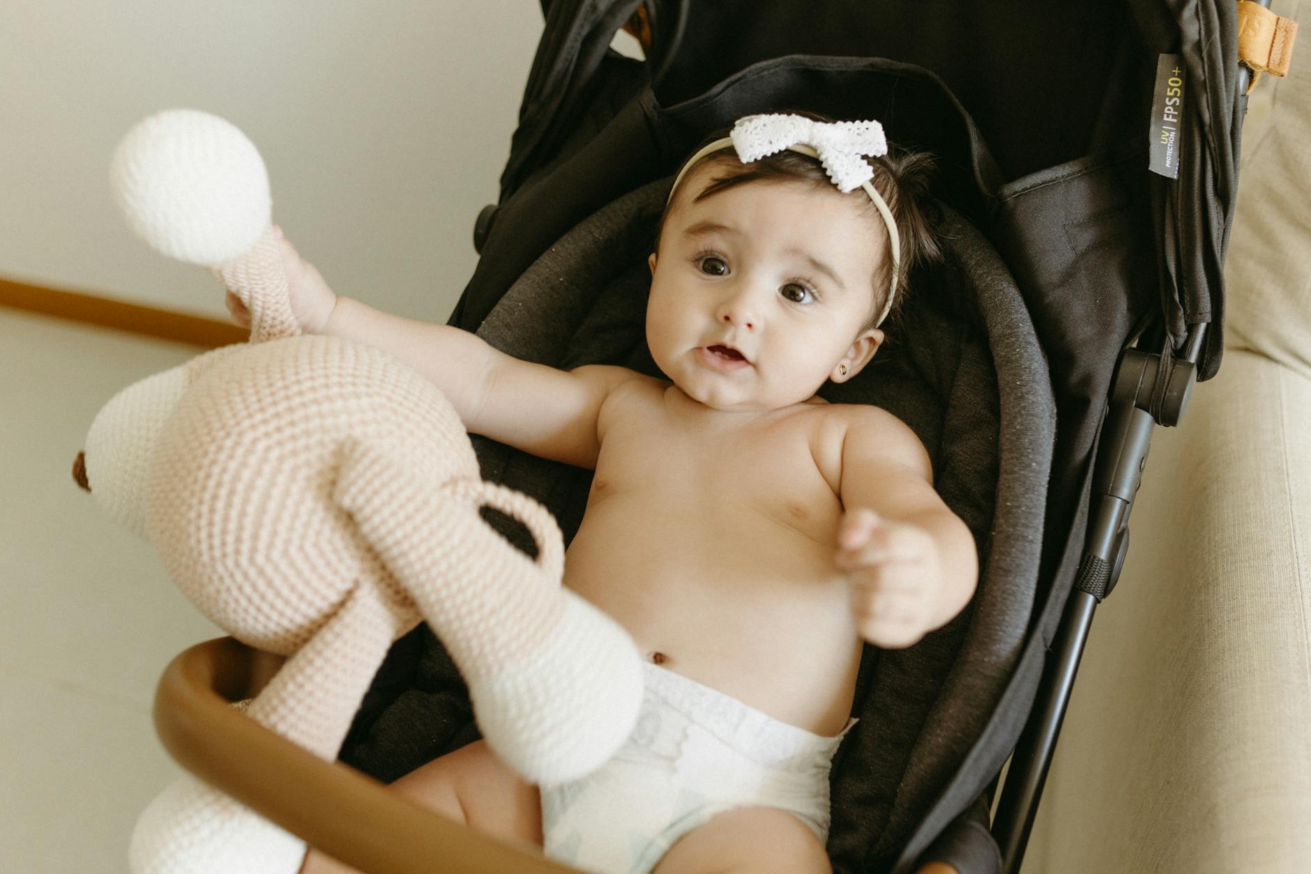 Uśmiechnięta niemowlęca dziewczynka w wózku trzymająca szydełkową zabawkę