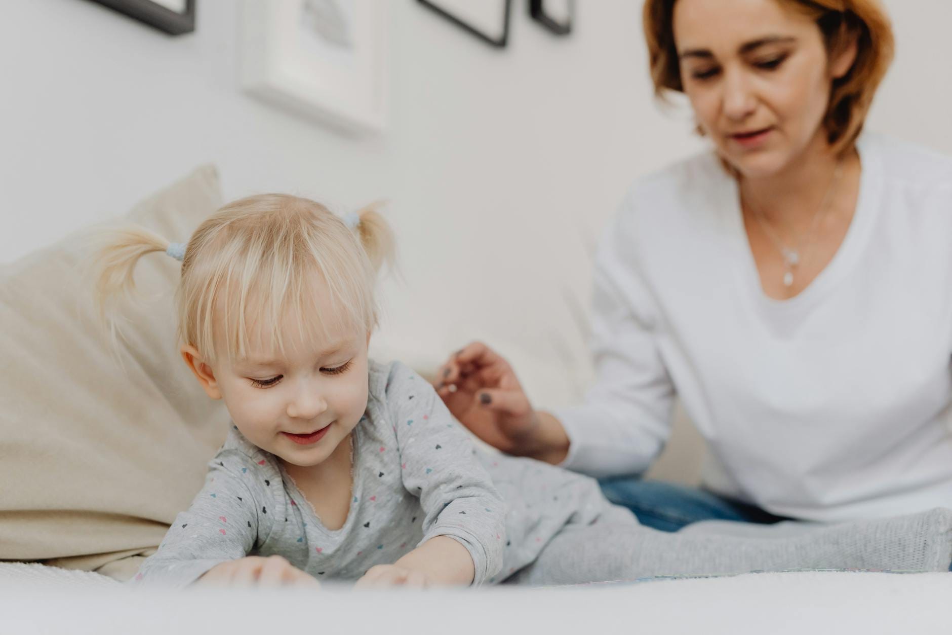Małe dziecko z kucykami bawi się w domu, mama obserwuje z uśmiechem