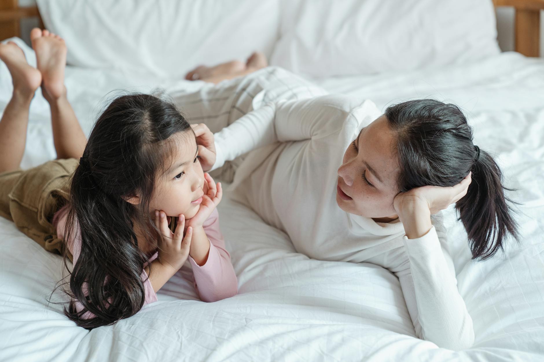 Mama leżąca z córką na łóżku, rozmawiają i spędzają czas razem