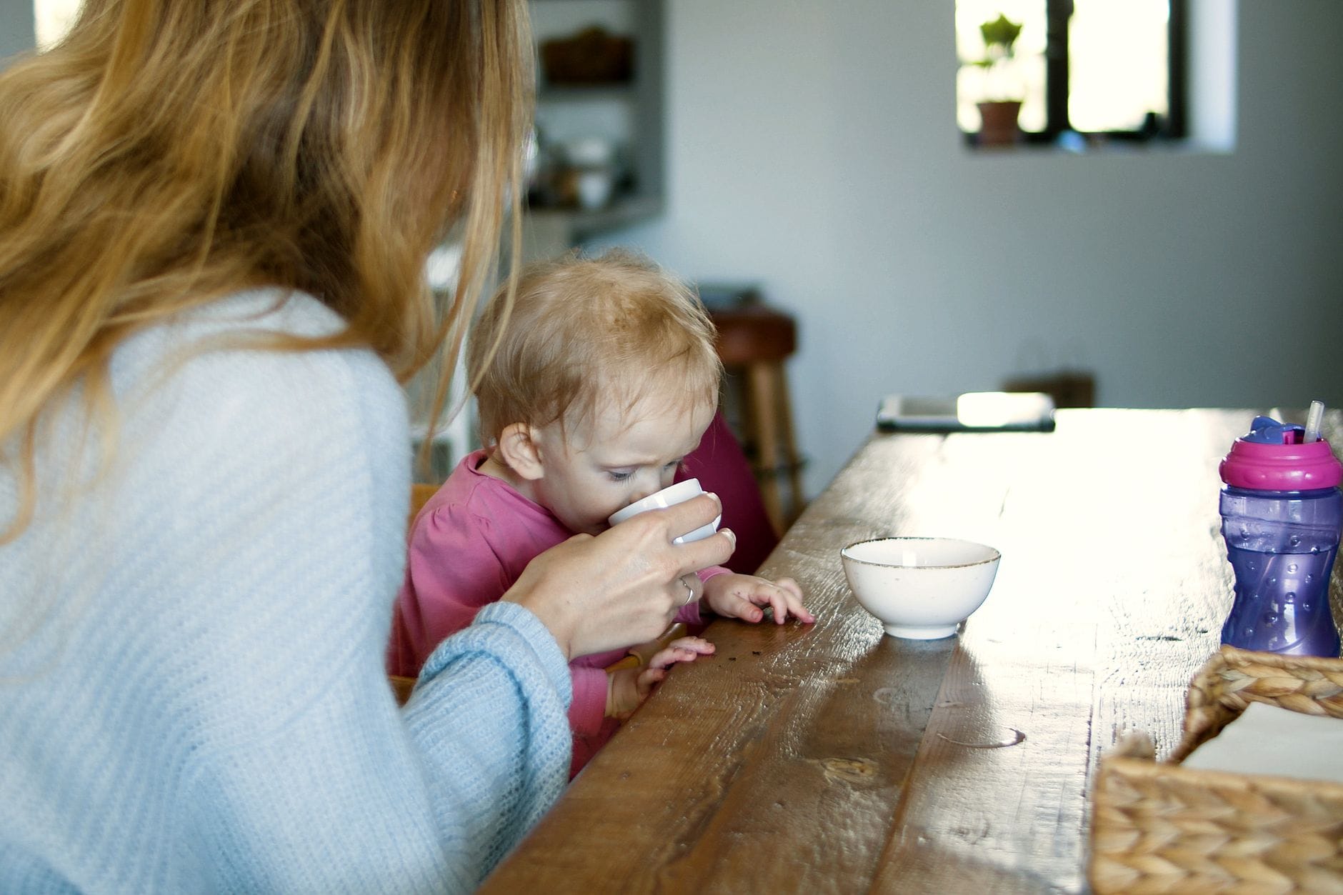 Trudne poranki jak zorganizować wyjście do przedszkola bez nerwów Mama pomaga dziecku pić z kubka przy kuchennym stole rano