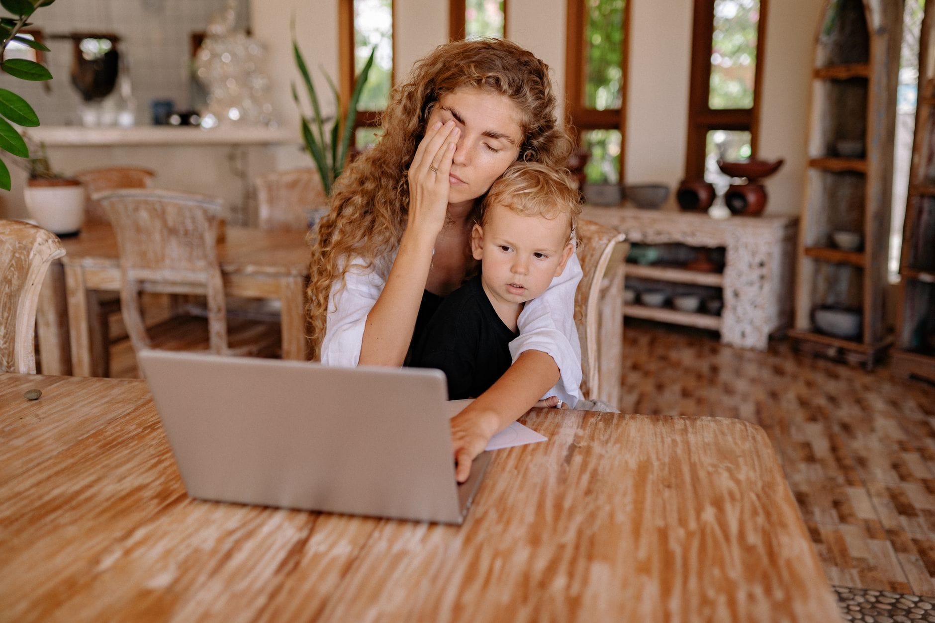 Mama pracuje przy laptopie w domu, obok bawi się jej dziecko
