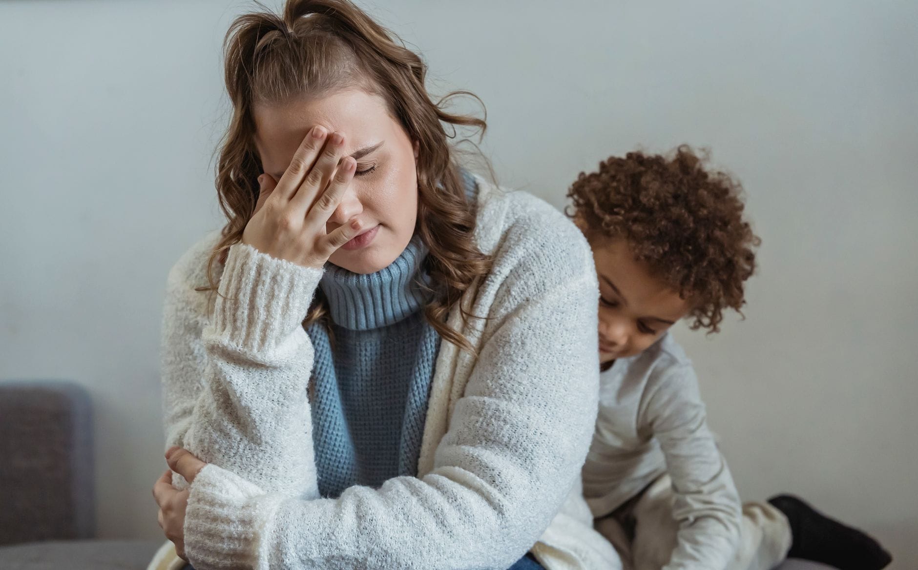 Zmęczona mama trzyma się za czoło obok smutnego syna w domu